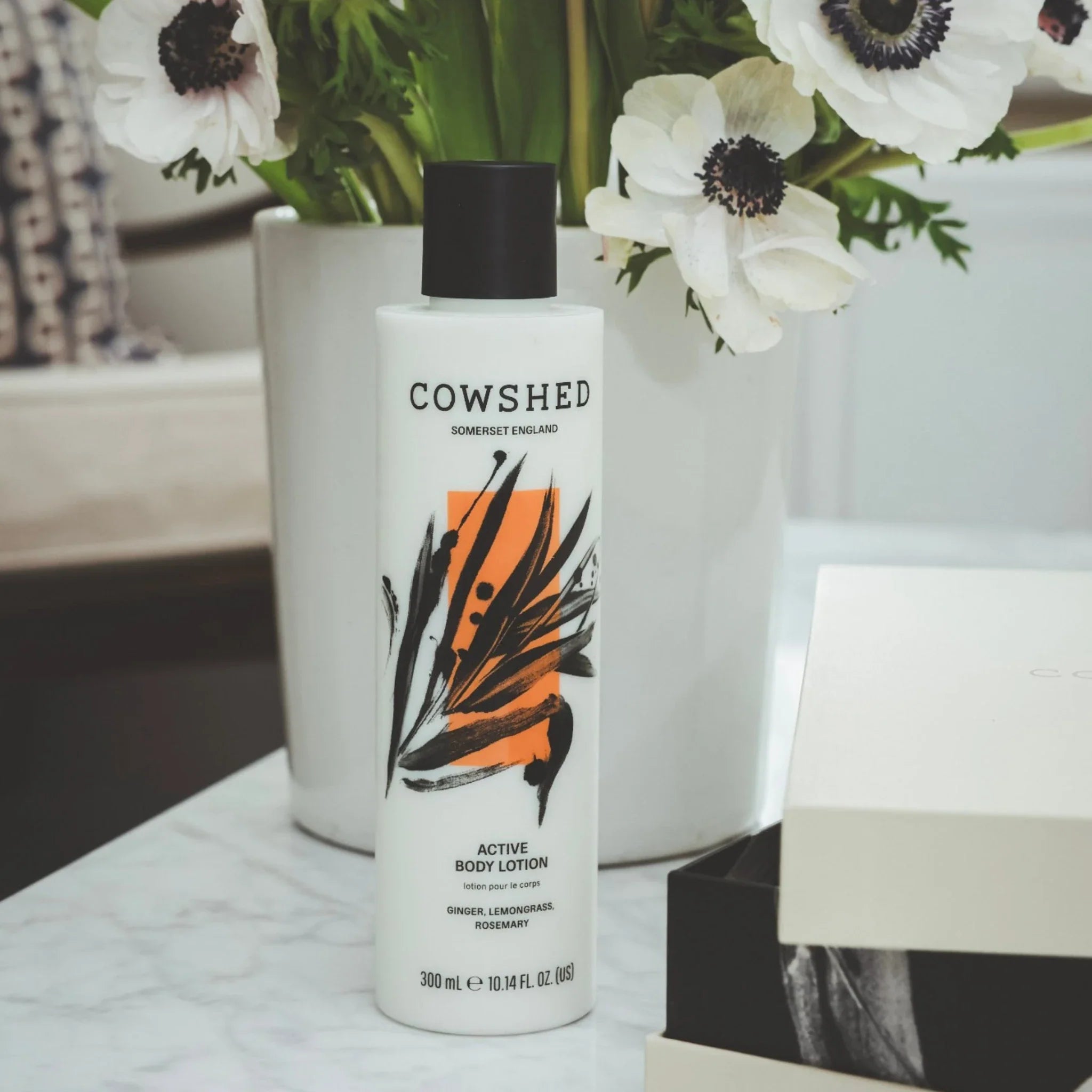 Cowshed Active body lotion bottle on a marble surface with flowers in the background