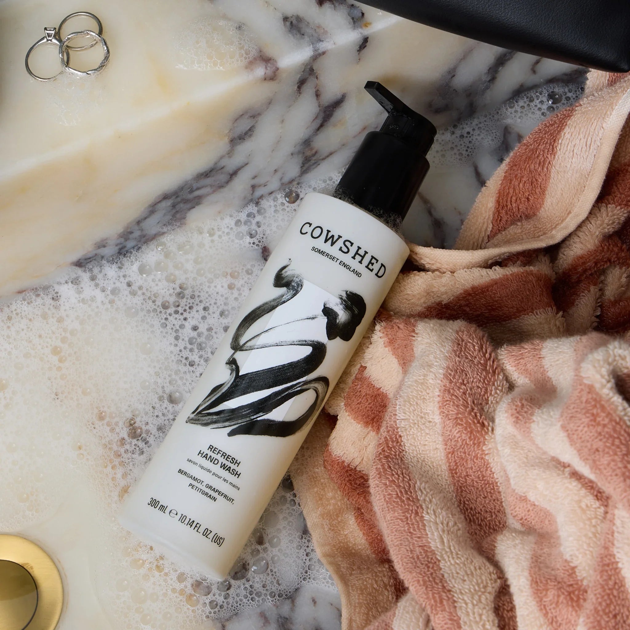 Cowshed Refresh hand wash 300ml bottle on a marble sink surface with soap and towel