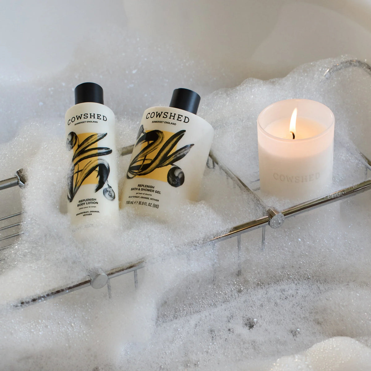 Two Cowshed bottles in a bubble bath with a lit candle.