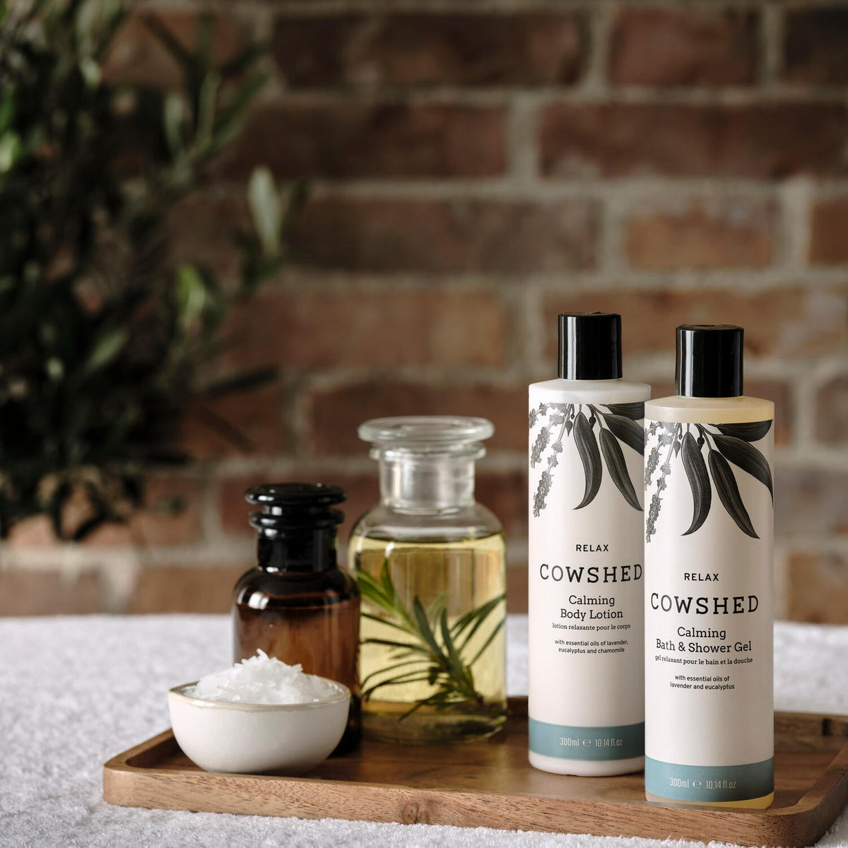 Cowshed skincare products on a wooden tray with a brick wall background
