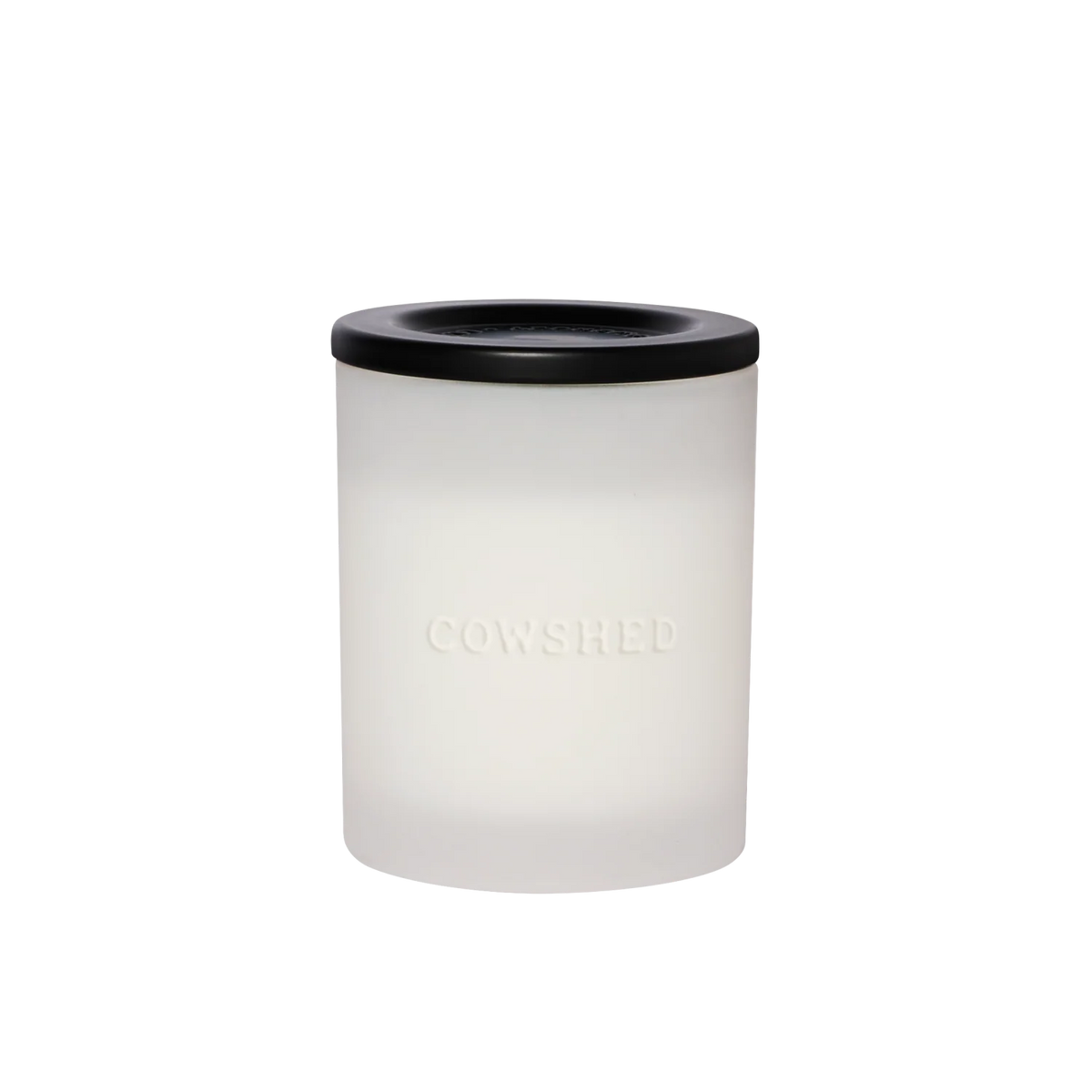 A frosted glass jar candle with a matte black lid, featuring the brand name 'COWSHED' embossed on the front, set against a plain white background.
