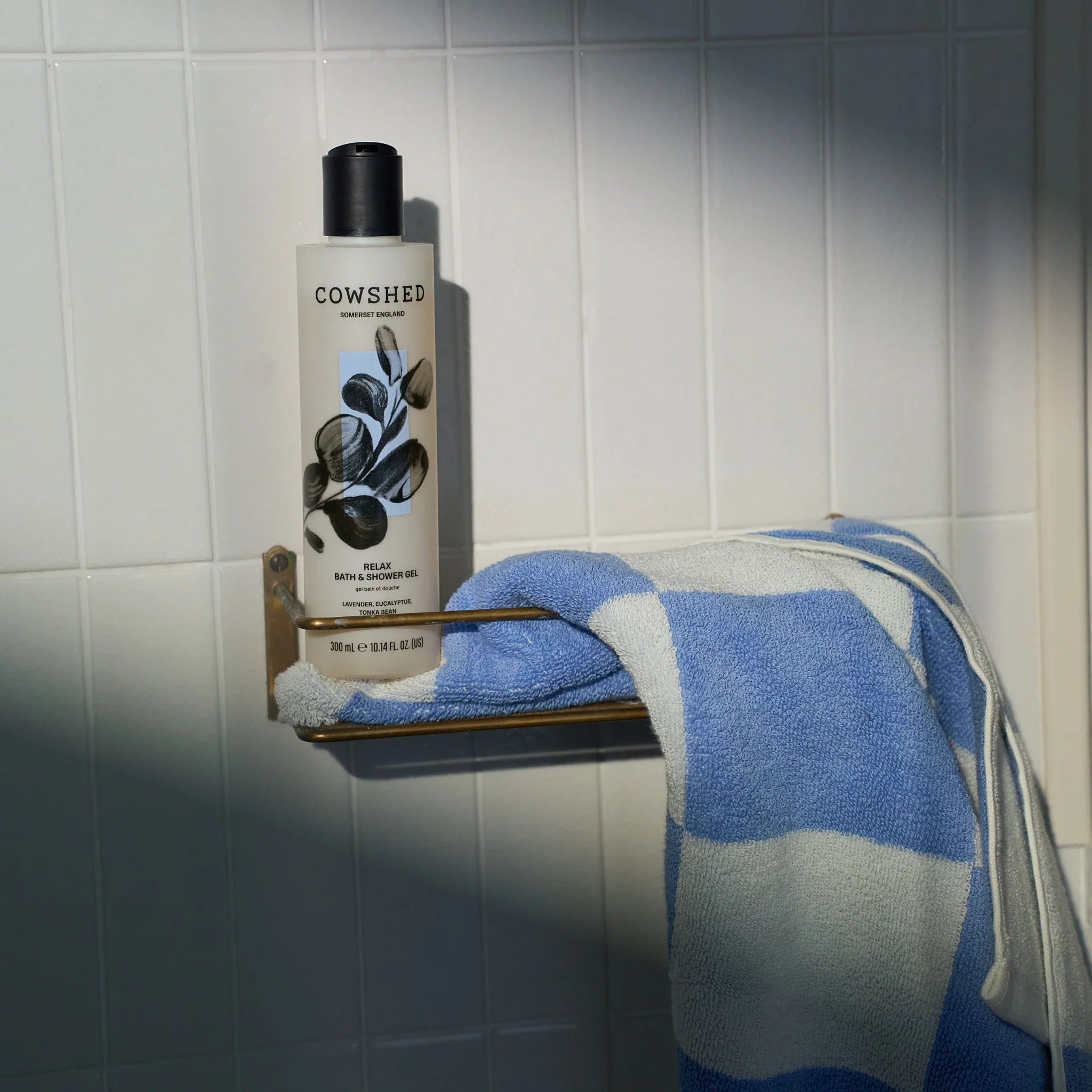 Cowshed Relax shower gel lavender & eucalyptus bottle on a towel rack with a blue and white towel