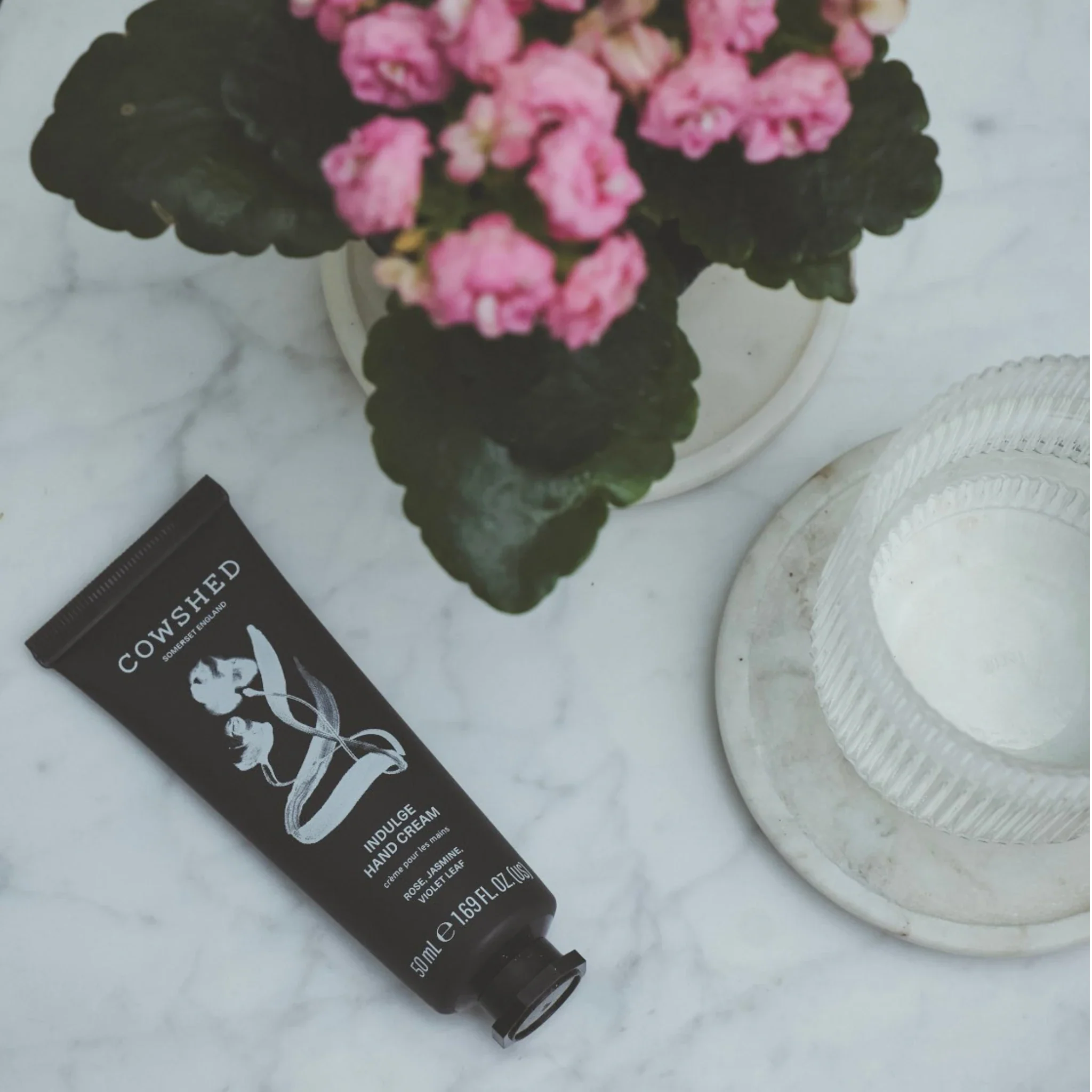 Cowshed hand cream tube on a marble surface with a potted plant in the background