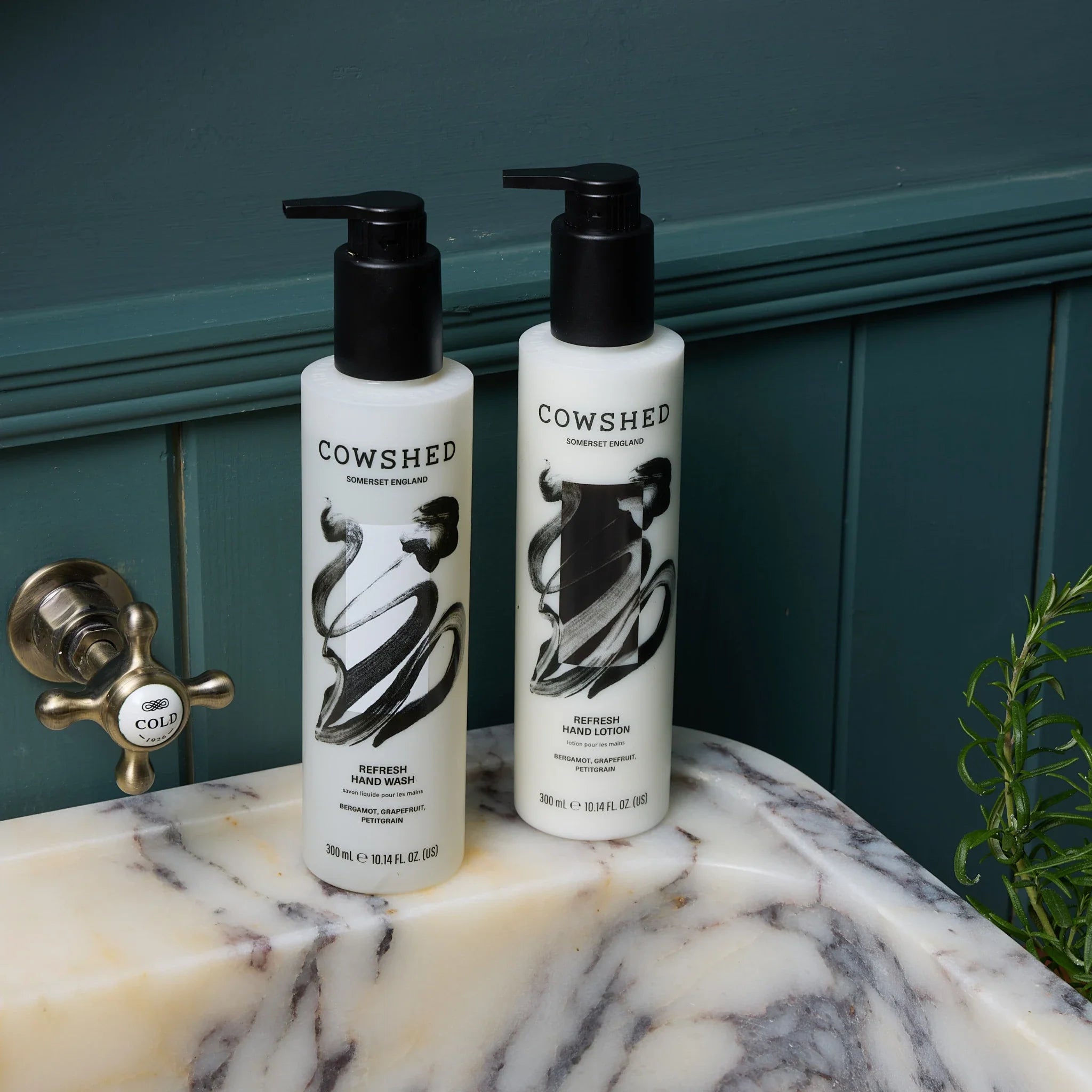 Cowshed hand wash & cream on a marble sink surface with a green panelled wall in the background.