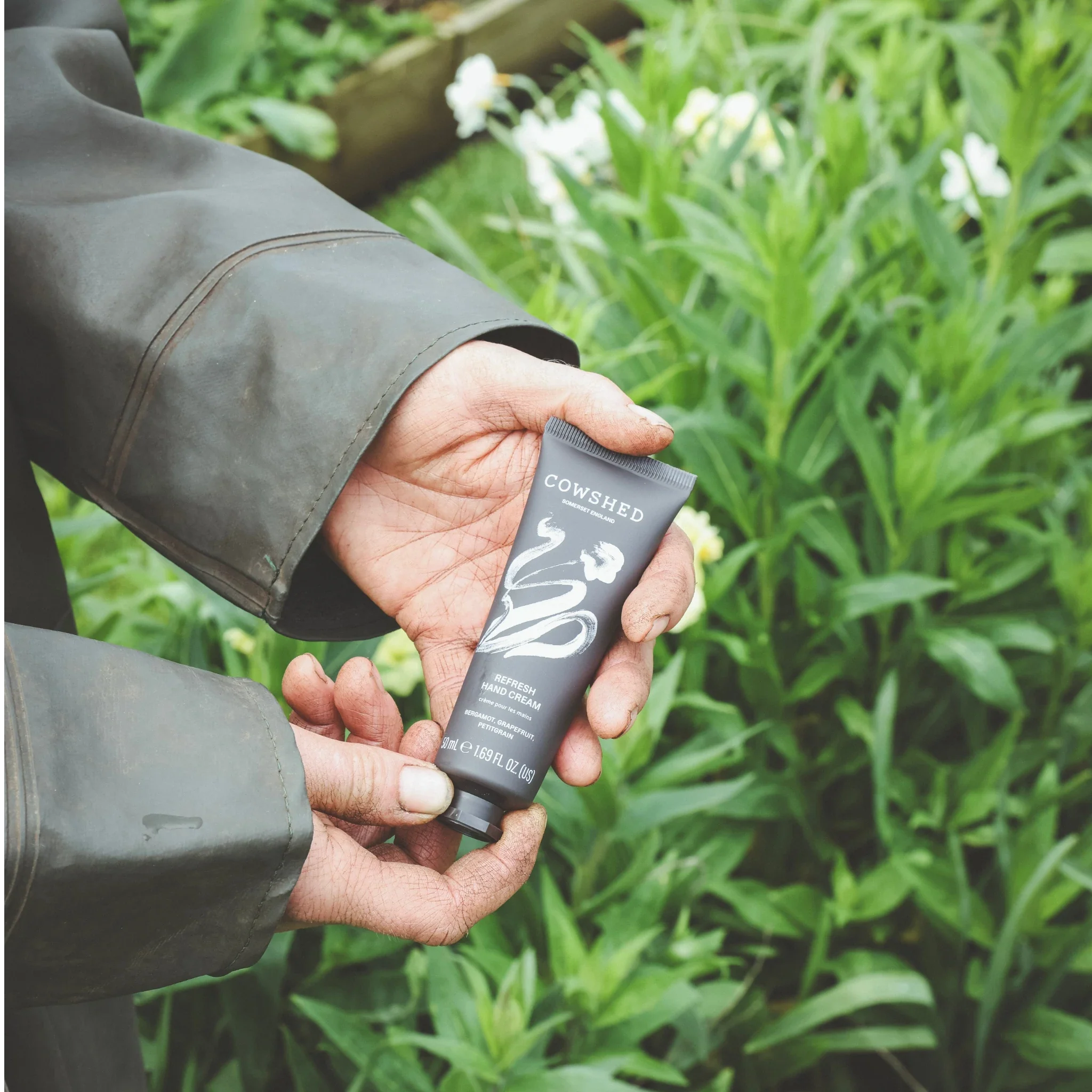 Person holding a tube of Cowshed Refresh hand cream in a British green garden