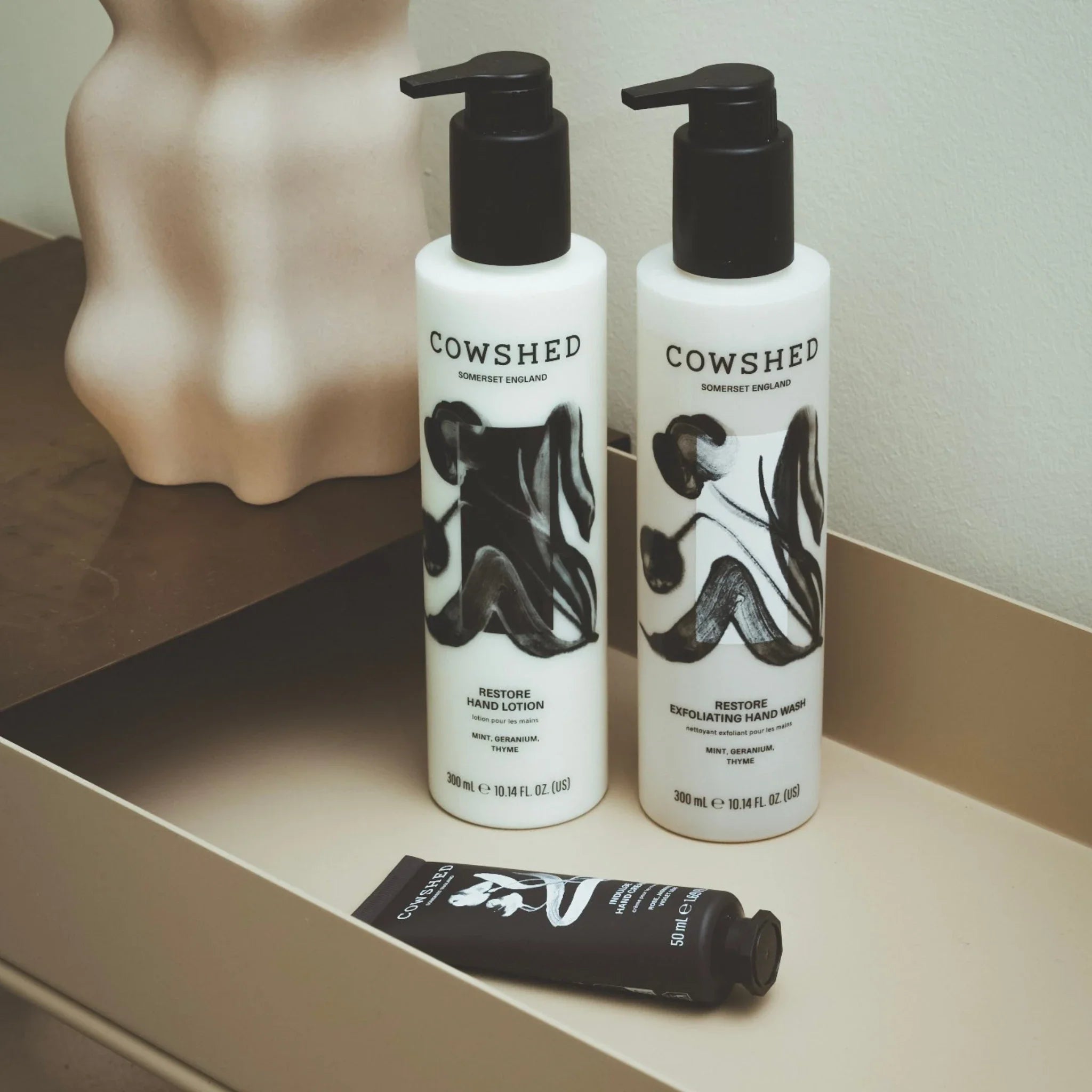 Two Cowshed hand care products on a shelf with a vase in the background.