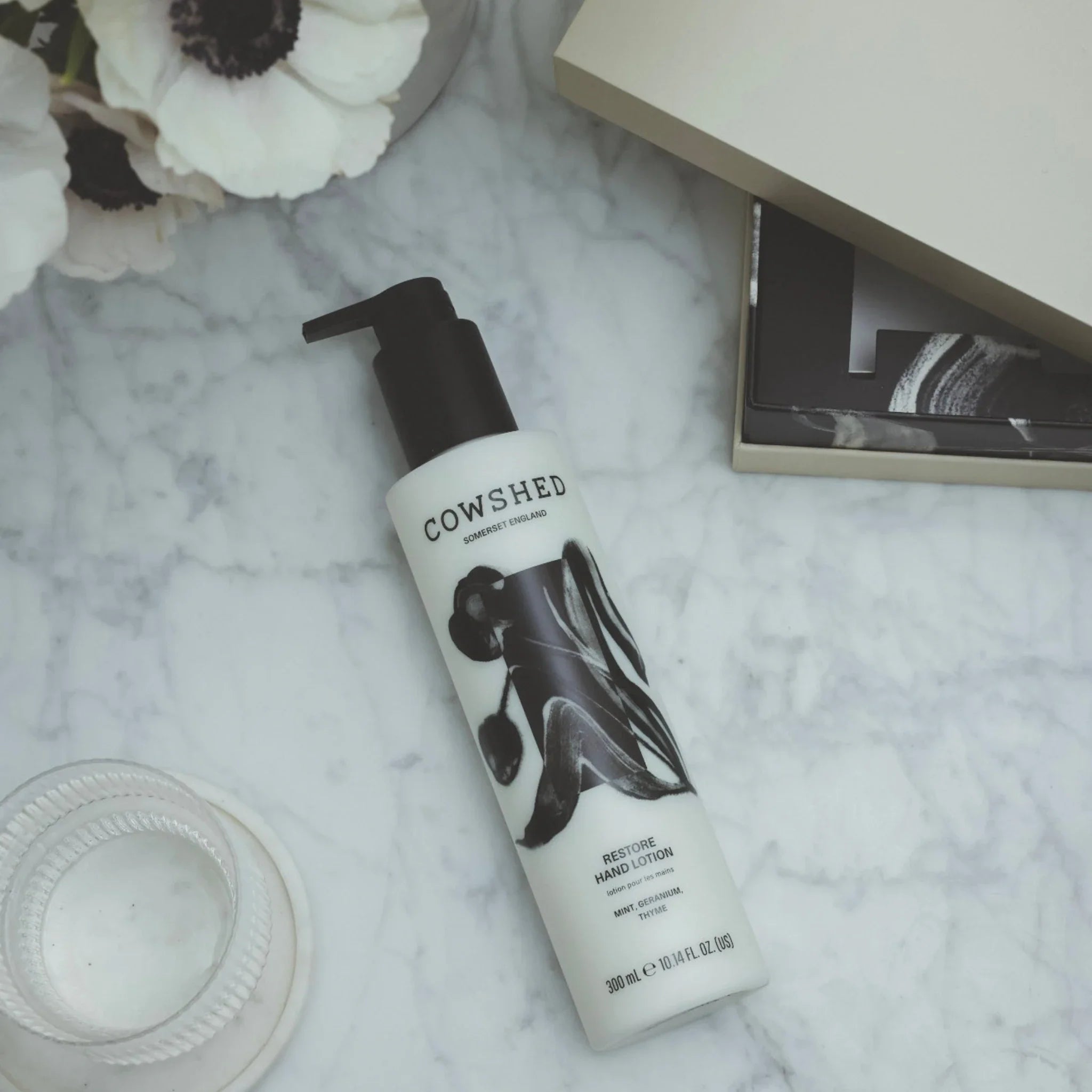 Cowshed product on a marble surface with flowers and a book in the background