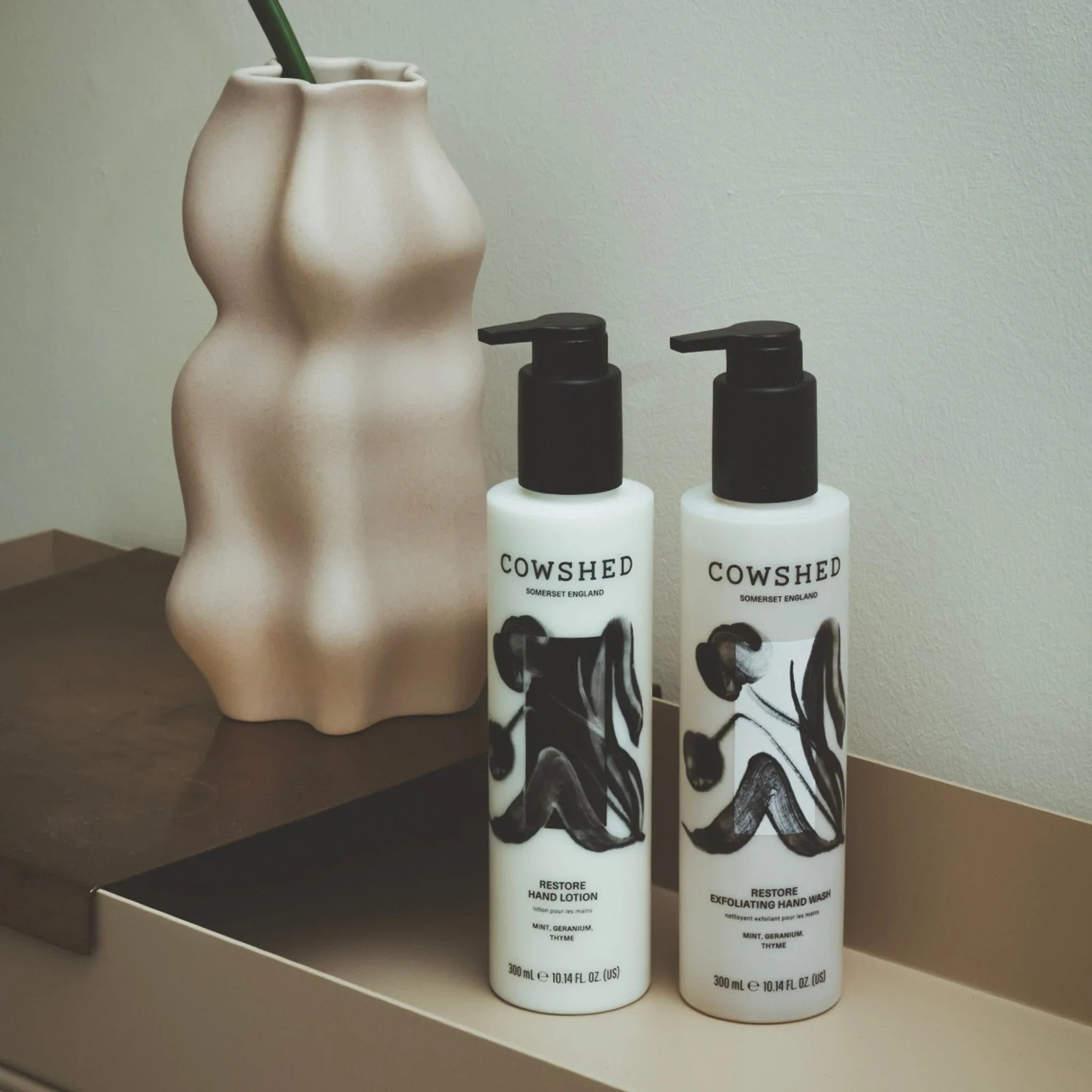 Two Cowshed bottles on a shelf with a decorative vase in the background.