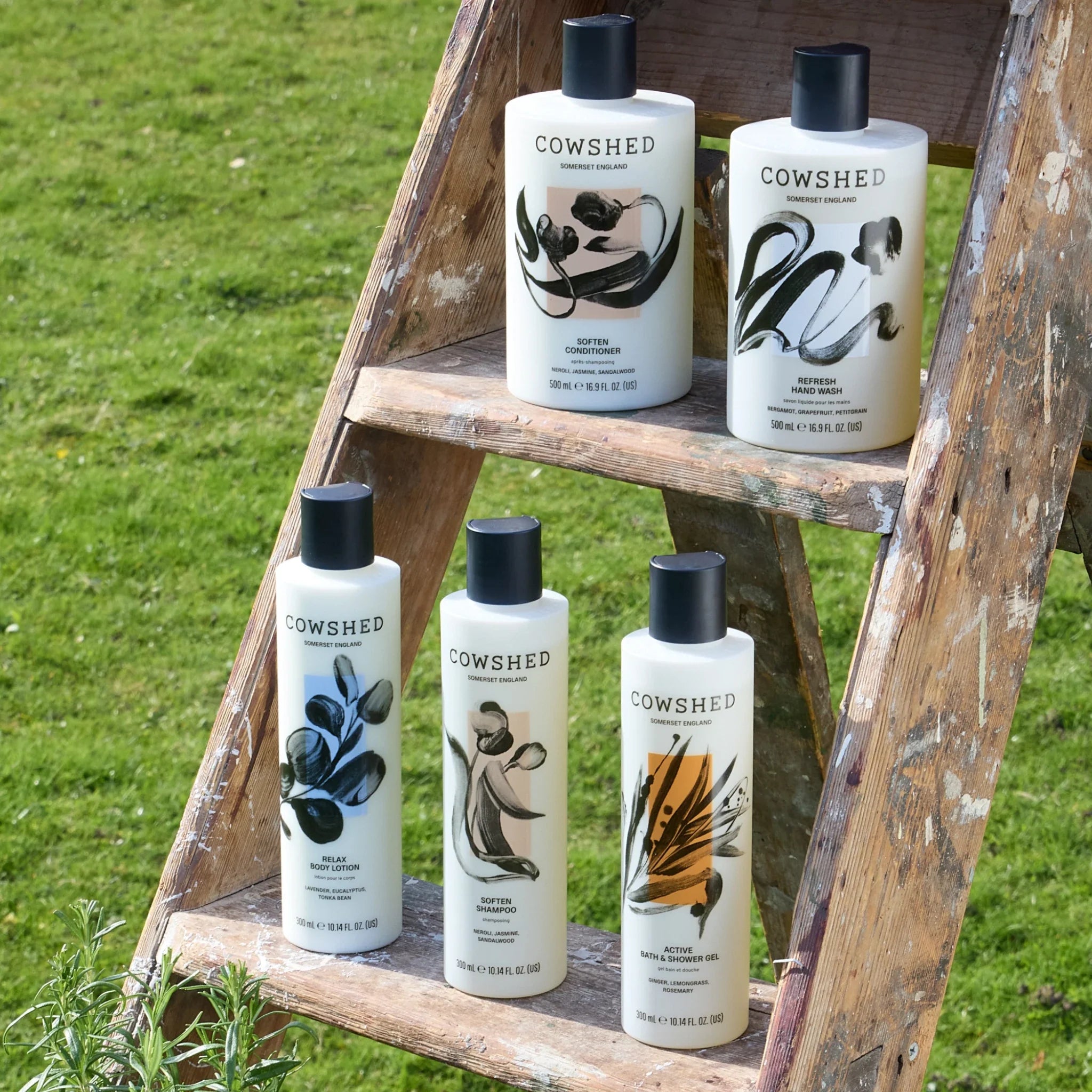 Selection of Cowshed product bottles on wooden ladder in a grassy field.