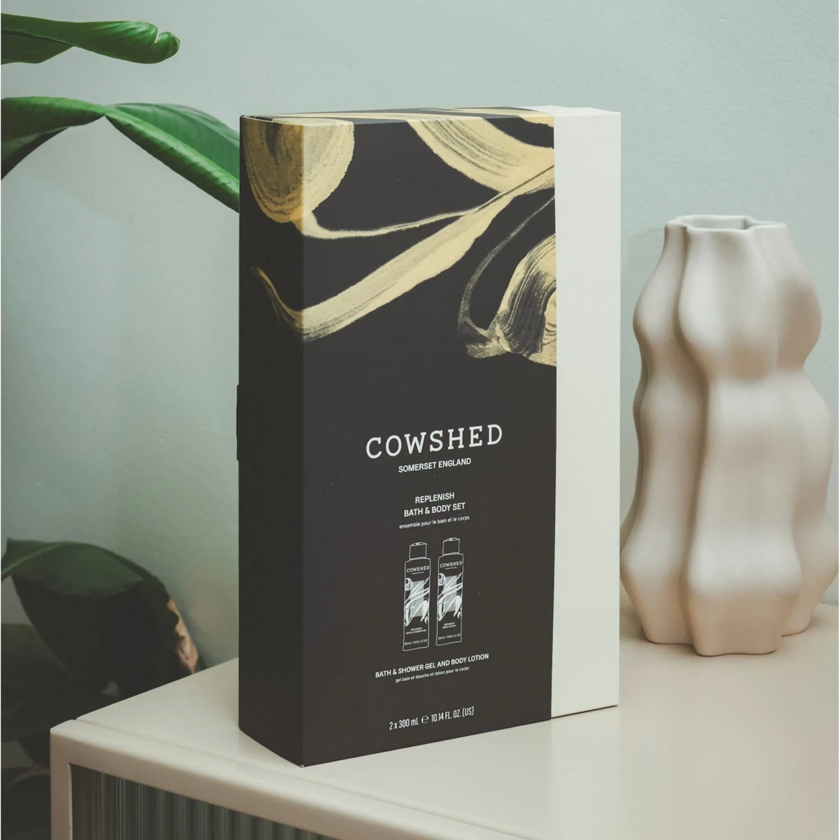 Cowshed product packaging on a table with a plant and vase in the background