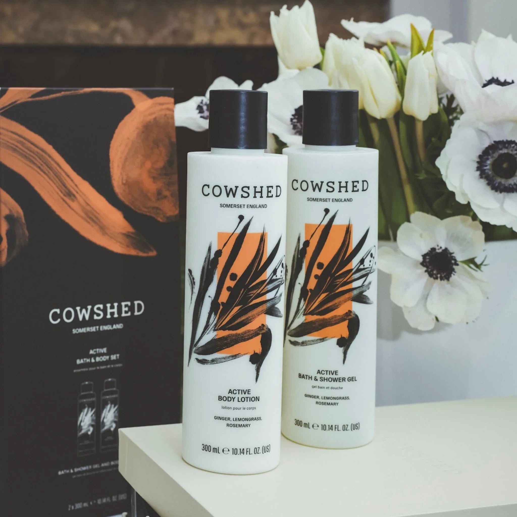 Two Cowshed bottles on a table with flowers in the background