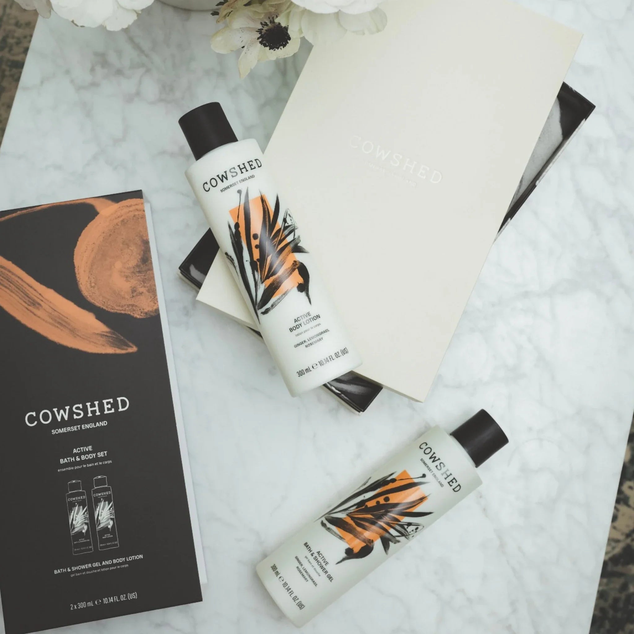 Cowshed body care products on a marble surface with flowers.