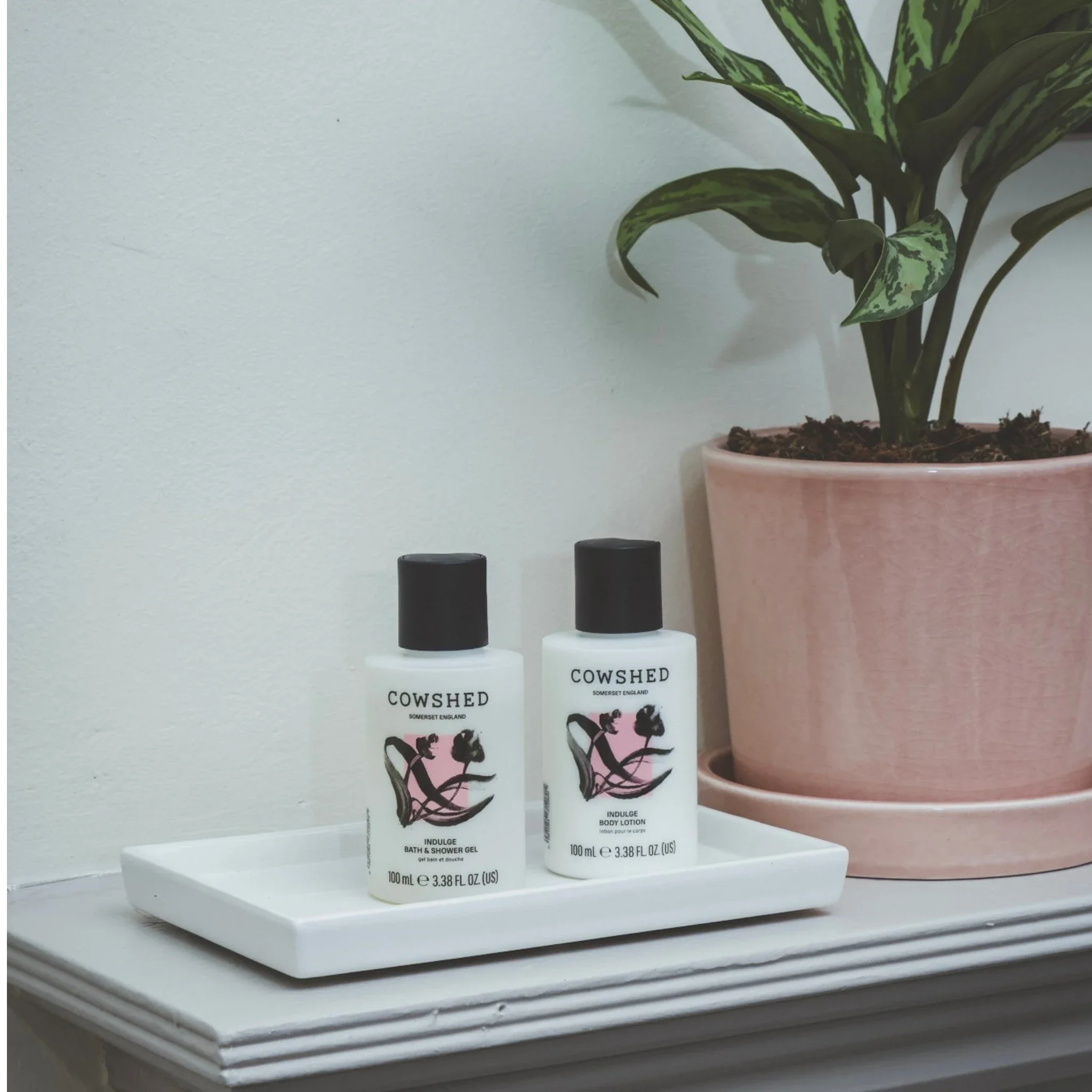 Two bottles of Cowshed products on a white surface with a plant in the background.