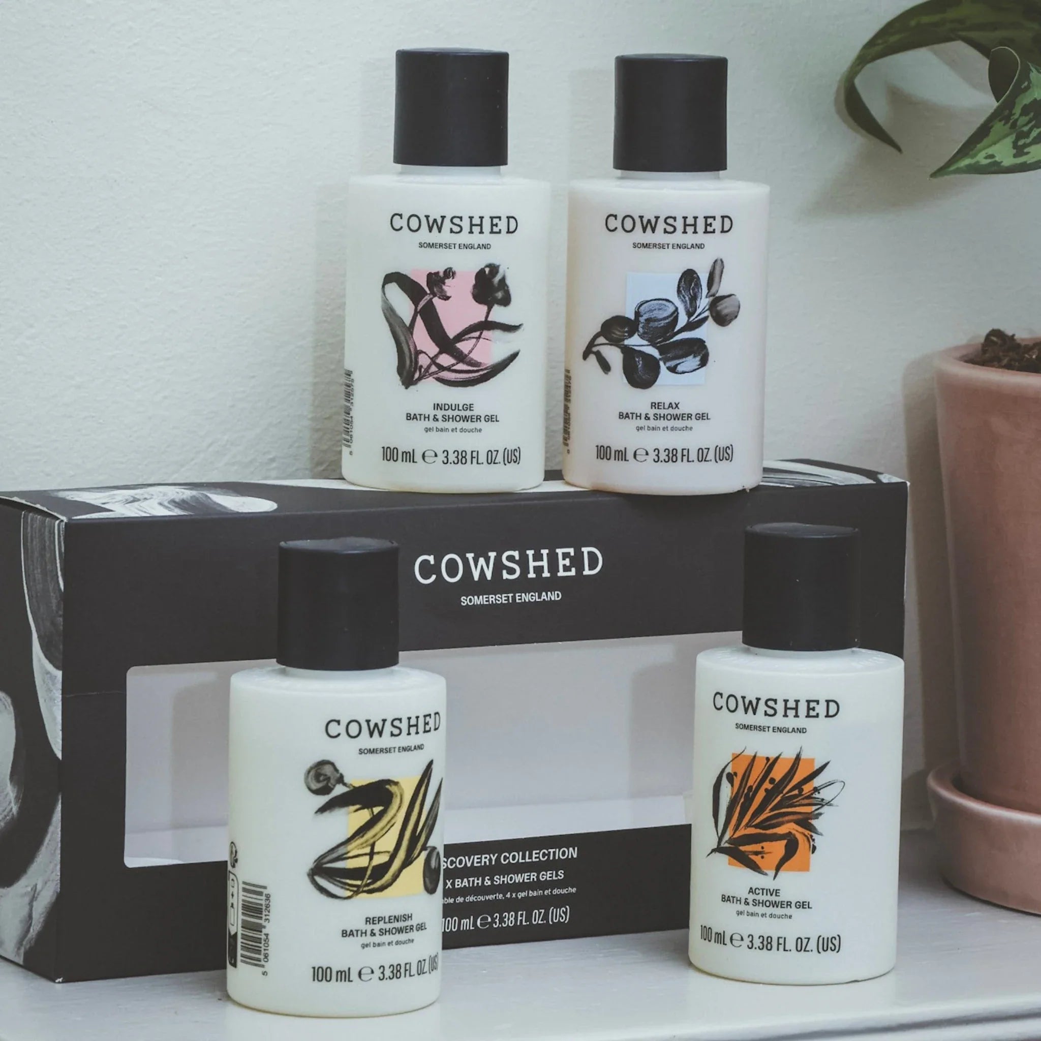 Cowshed bath and shower gel bottles on a white surface with a plant in the background