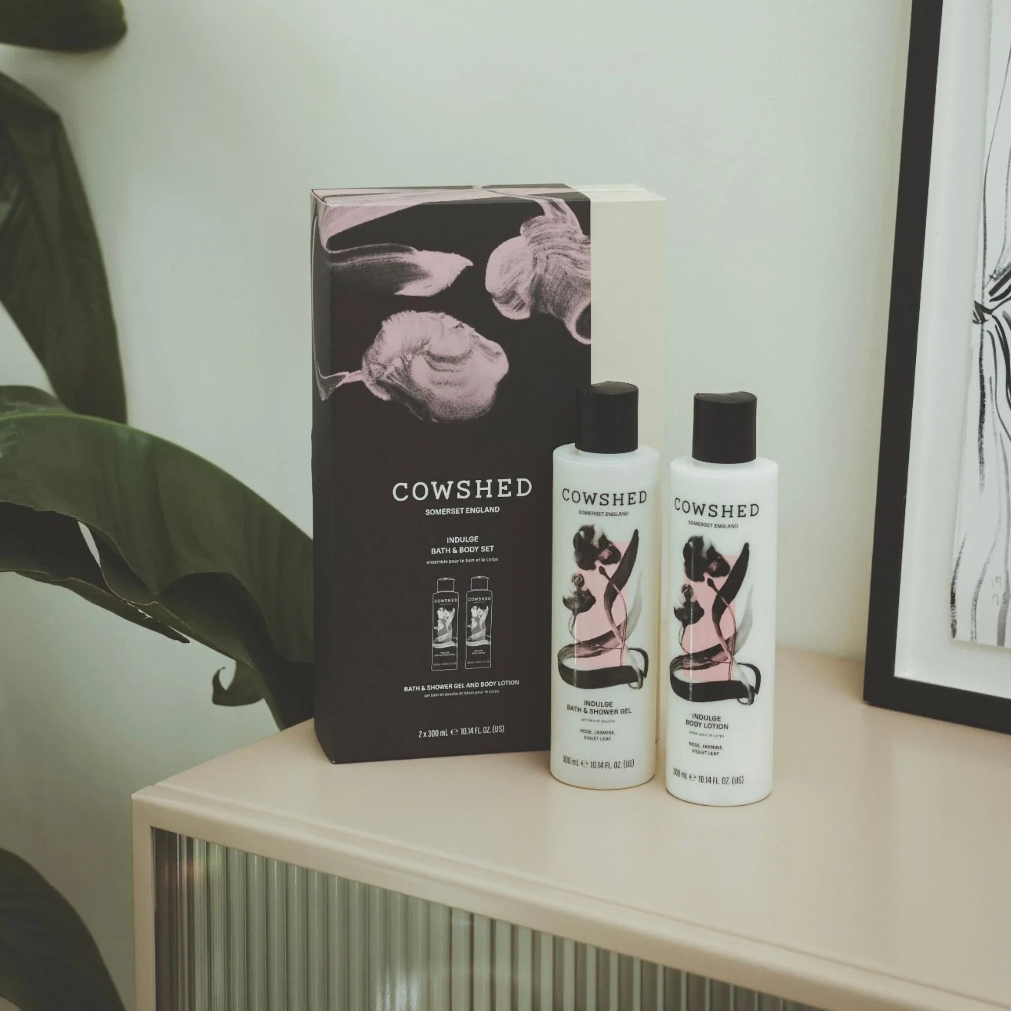 Cowshed skincare products on a shelf with a plant and framed picture in the background