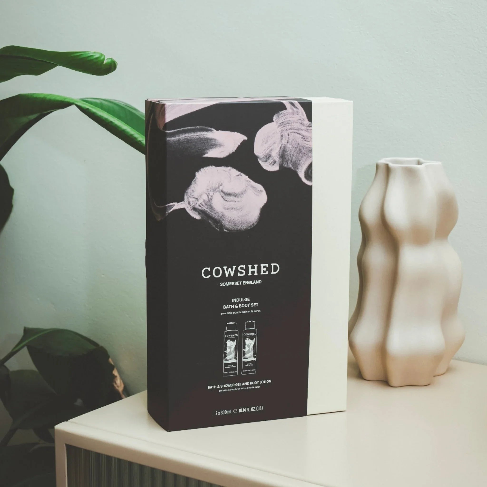 Cowshed product packaging on a shelf with a plant and vase in the background