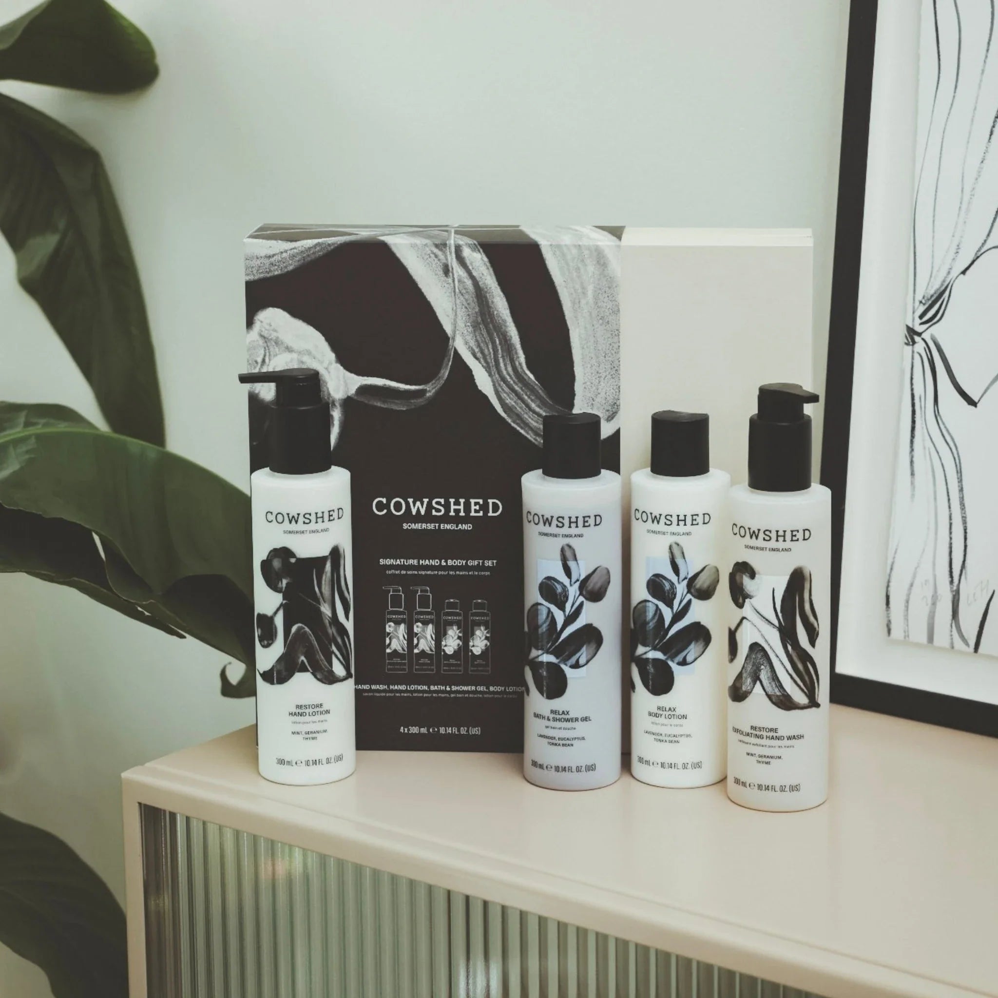 Cowshed skincare products on a shelf with a plant and abstract art in the background