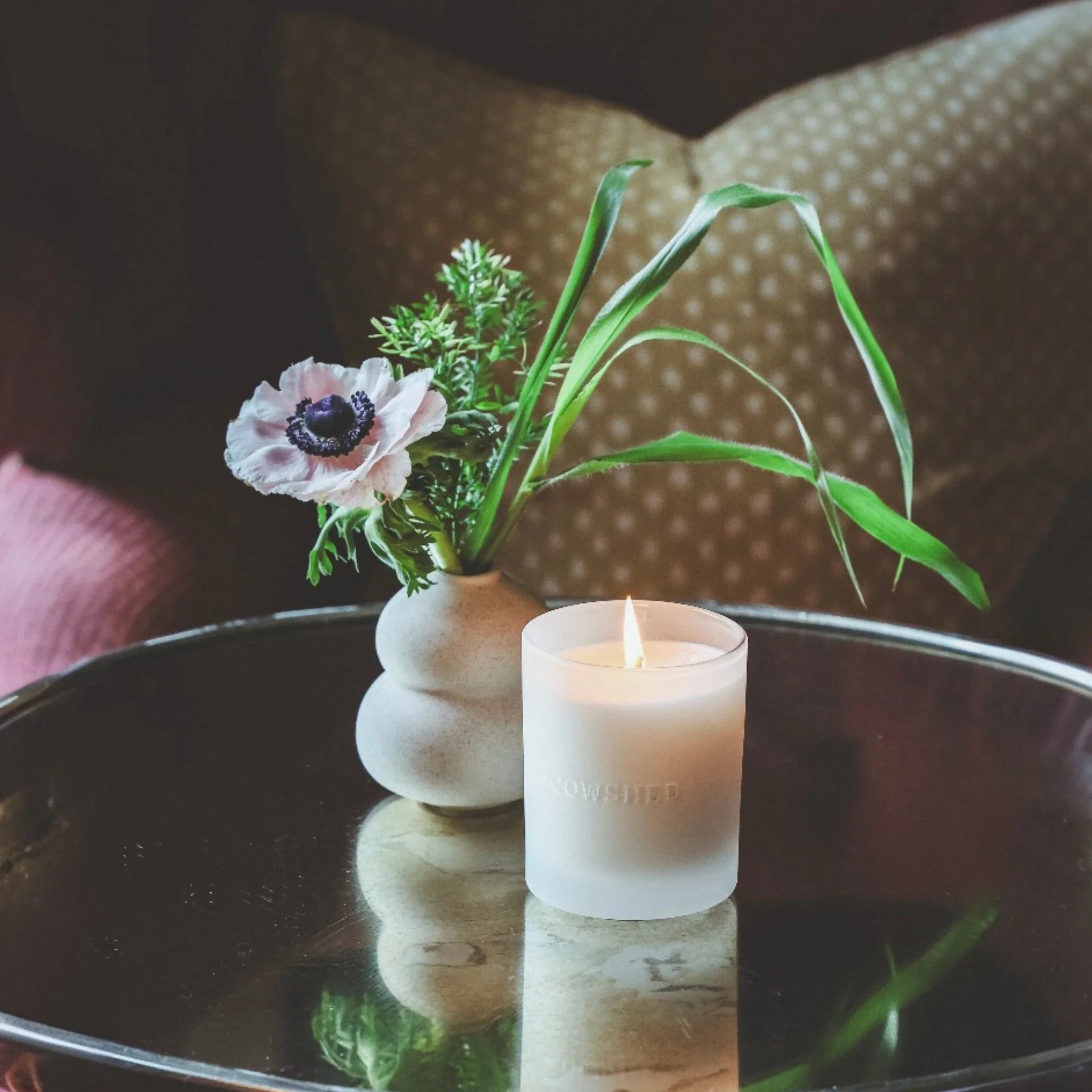 Cowshed candle and vase with flowers on a reflective surface