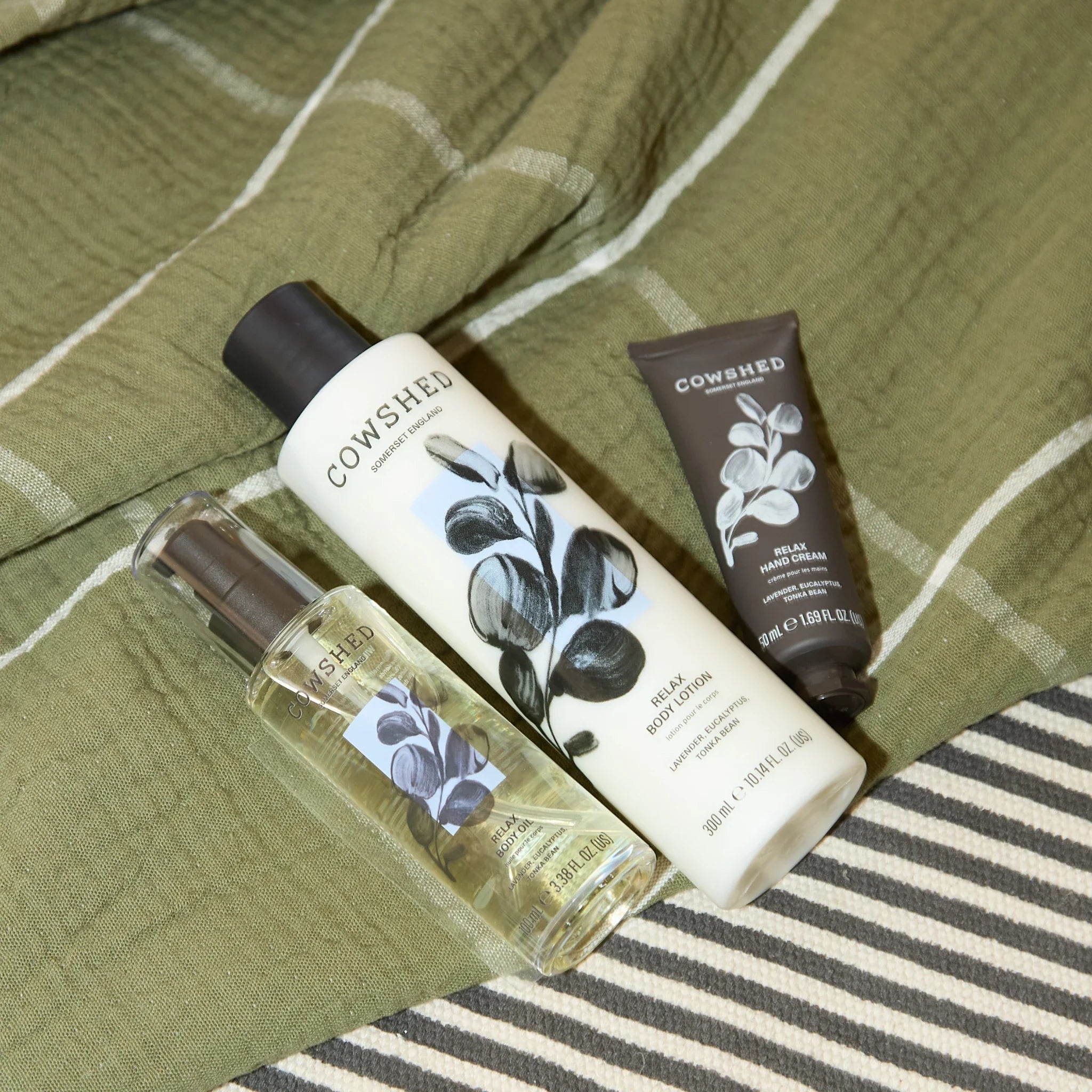 Cowshed skincare products on a green and white striped fabric background