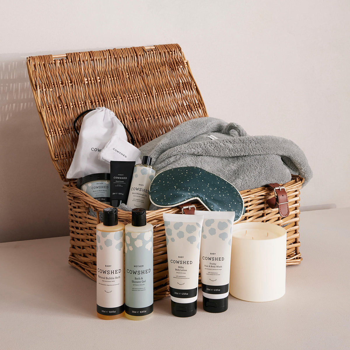 A wicker hamper with the lid open, displaying various baby and mother care products, including bottles and skincare items.
