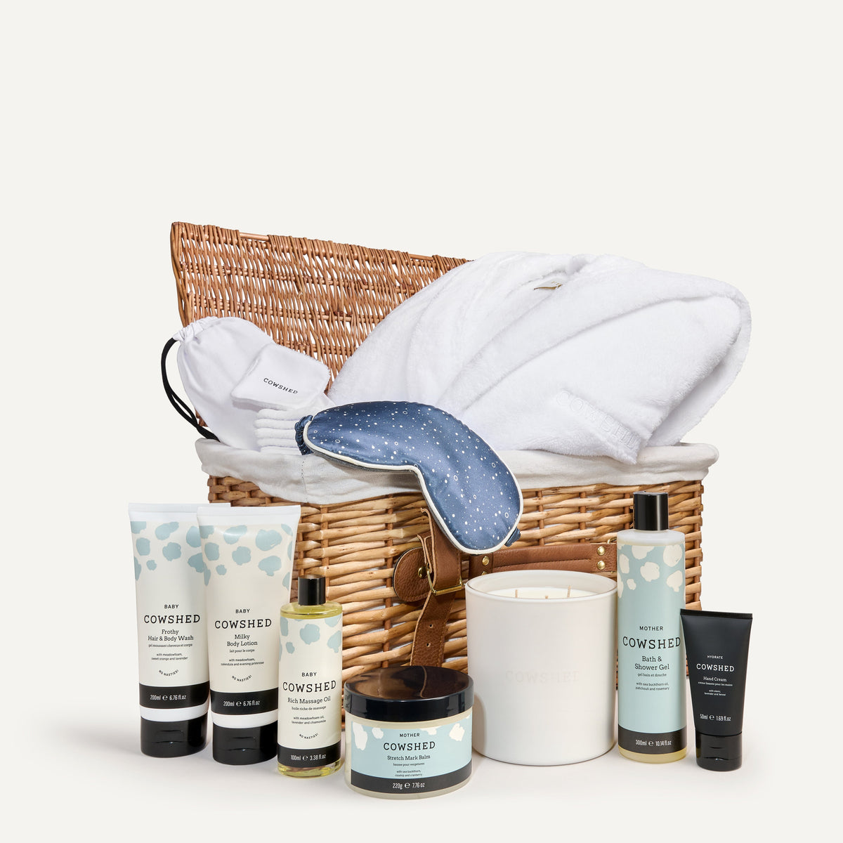 Cowshed product set including candles, bottles, and a towel in a wicker basket on a white background
