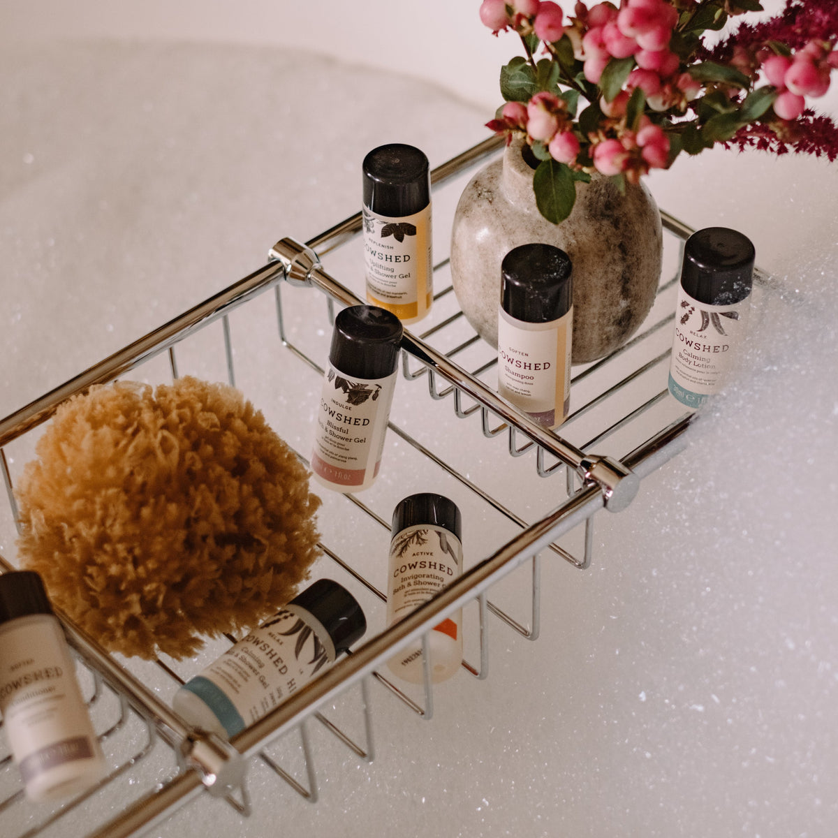 Bath caddy with cowshed shower gels, a sponge, and flowers in a bathtub.