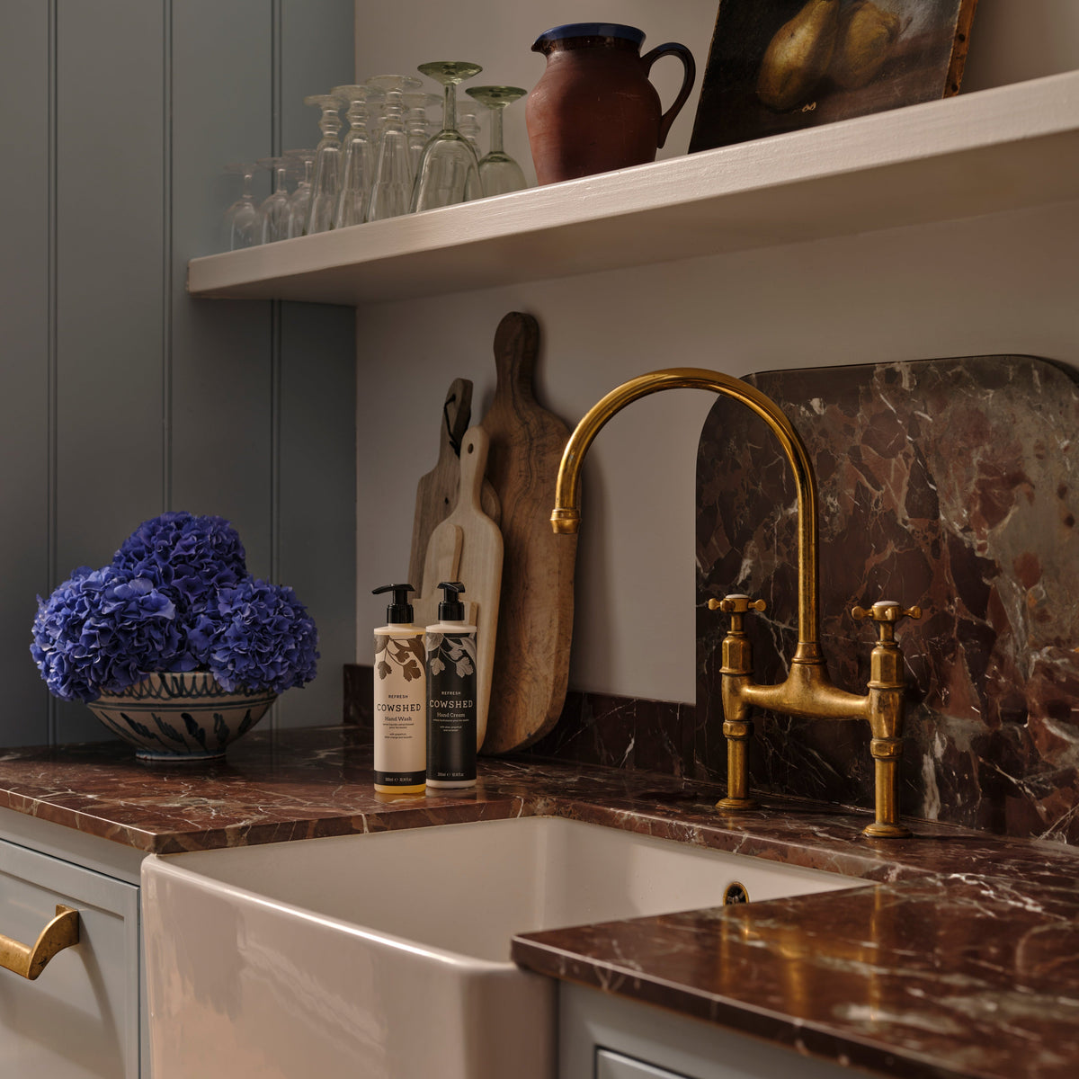 Kitchen sink area with marble countertop, gold faucet, and various Cowshed hand care products