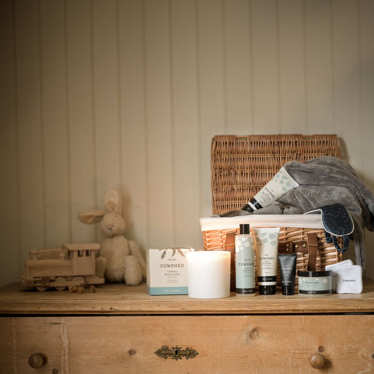 Cosmetic products on a wooden dresser with a wicker basket and plush toy in the background.