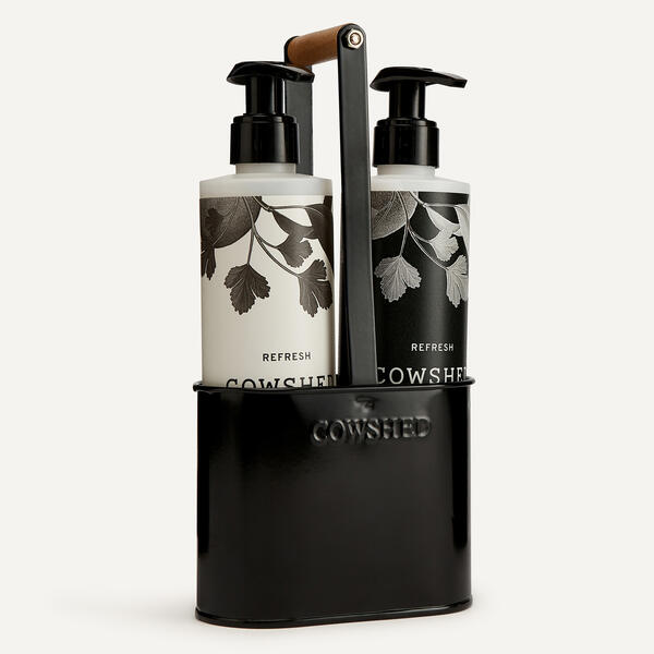 A black metal hand care caddy with a handle, containing two pump bottles labeled 'REFRESH' and 'COWSHED'.
